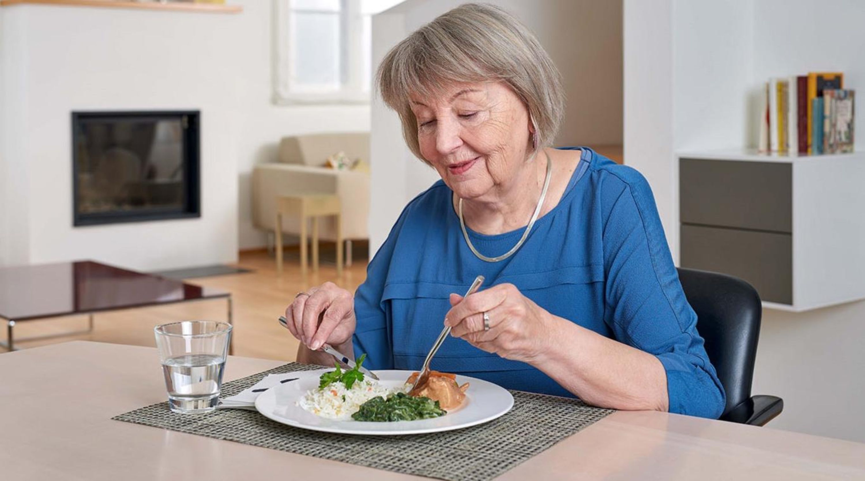 Un’anziana consuma il pasto seduta a tavola.