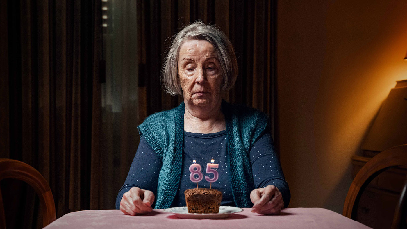 Une femme seule est assise à une table et regarde tristement son gâteau d'anniversaire.