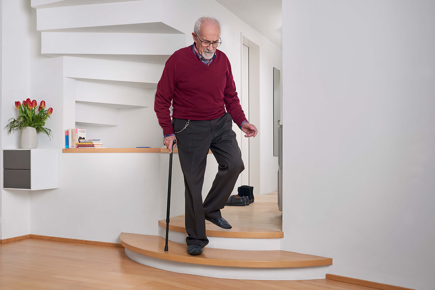 Un uomo anziano scende con cautela le scale con un bastone.