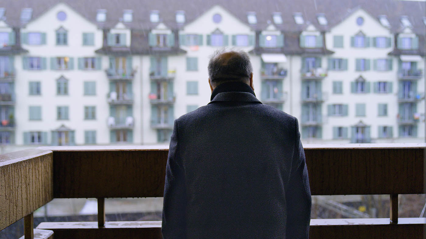 Un uomo è in piedi sul balcone e guarda una fila di case.