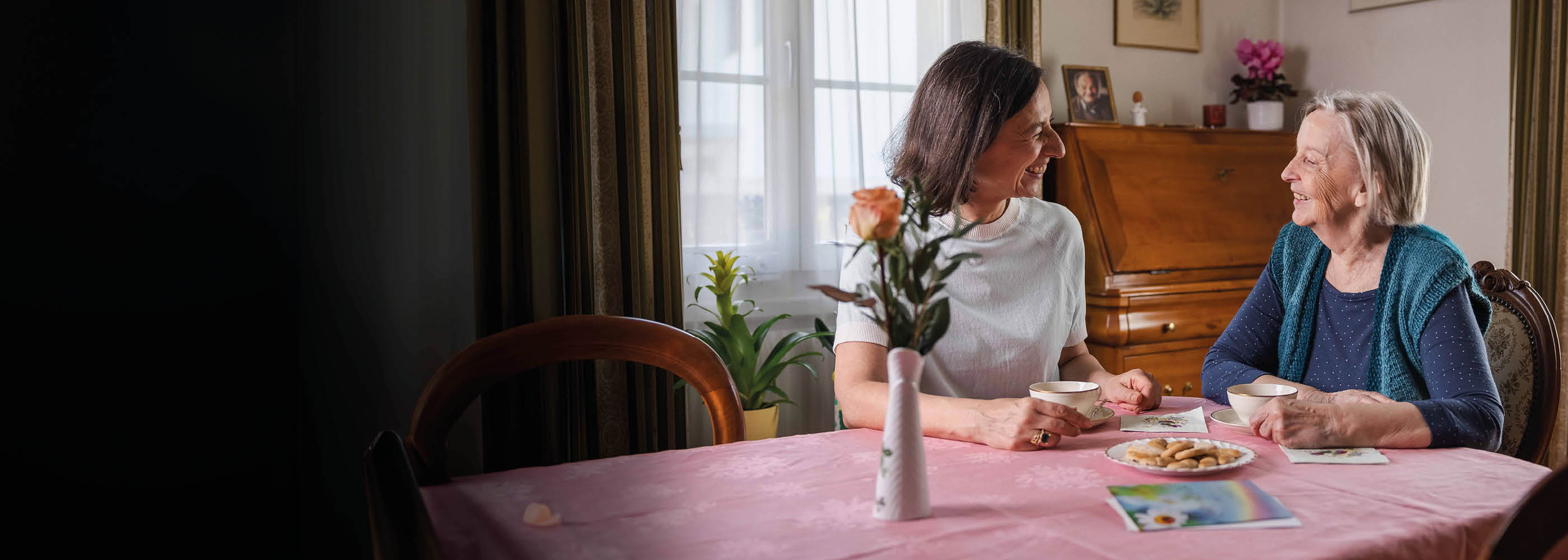 Une collaboratrice de Pro Senectute est assise à table avec une personne âgée autour d'un café et d'un gâteau.